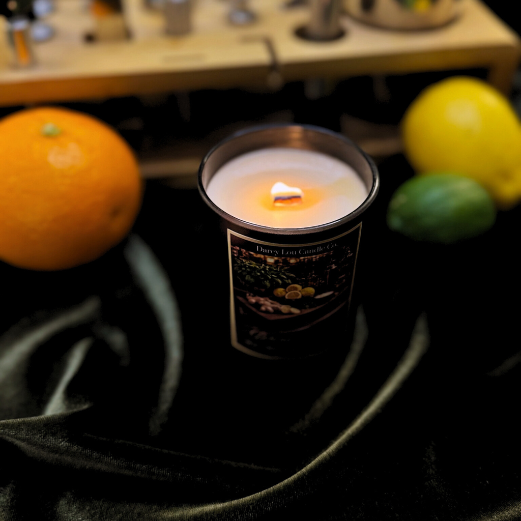Candle in a tin with a label, surrounded by fruits on a dark surface