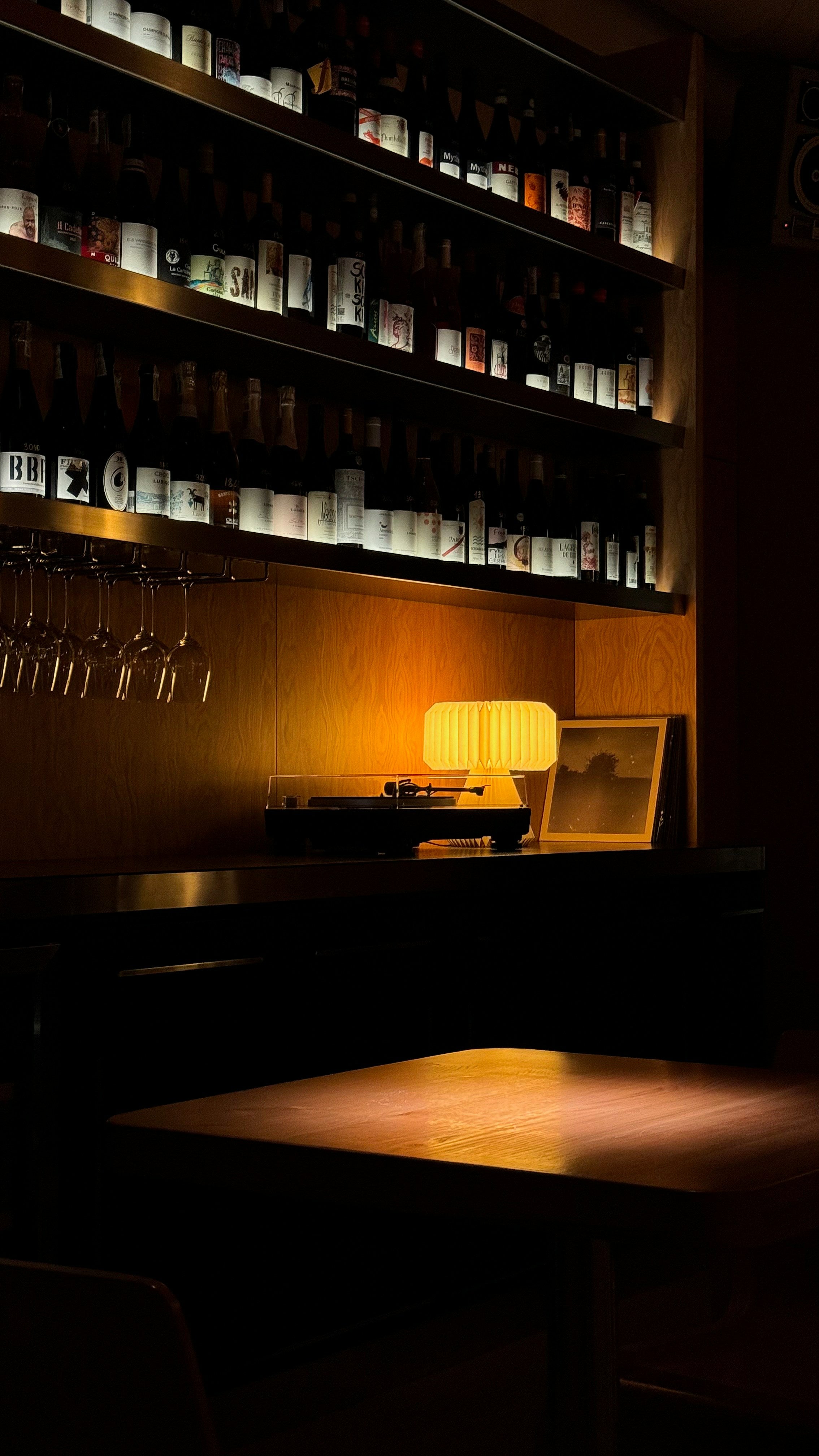 Dark bar setting with shelves of bottles and a lit lamp.