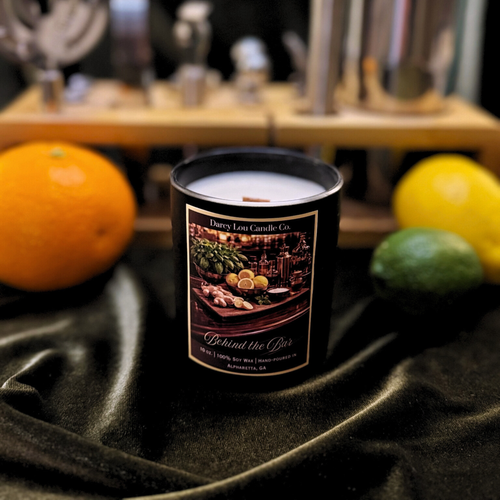 Candle with a label on a dark surface with fruits in the background