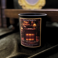 Candle with a label featuring a cozy interior scene on a dark surface.