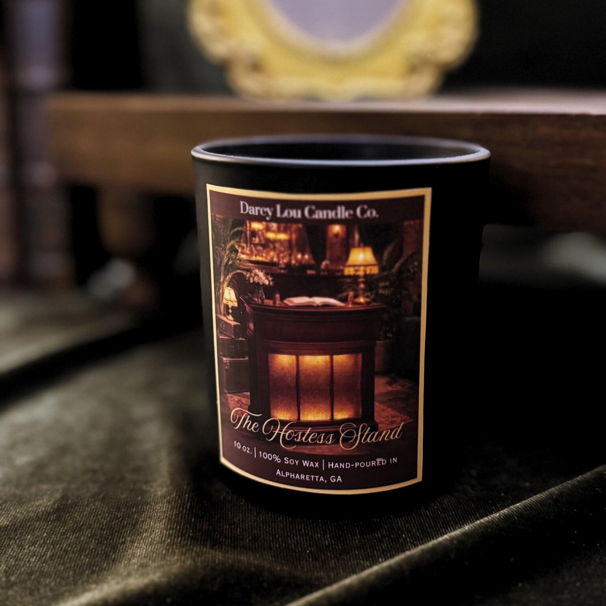 Candle with a label featuring a cozy interior scene on a dark surface.